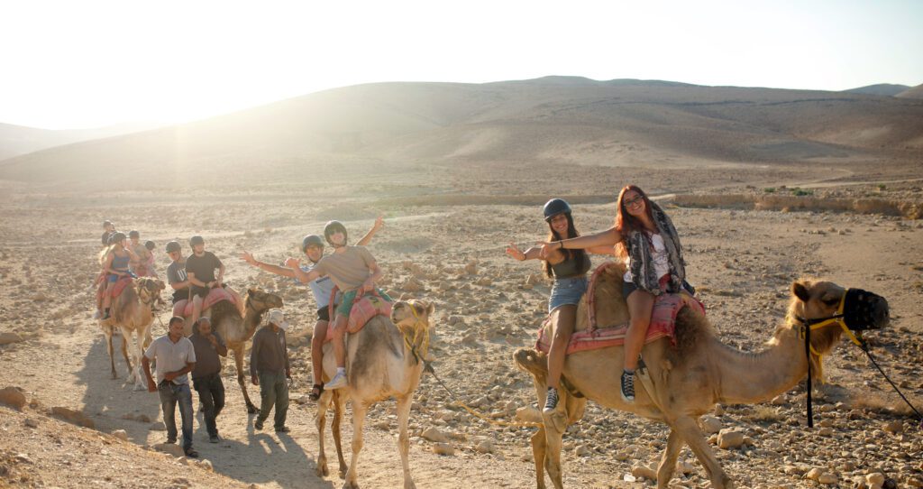 Teens riding camels through the desert in Israel.