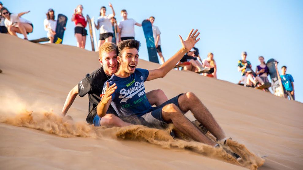 Smiling kids sliding down sand dune