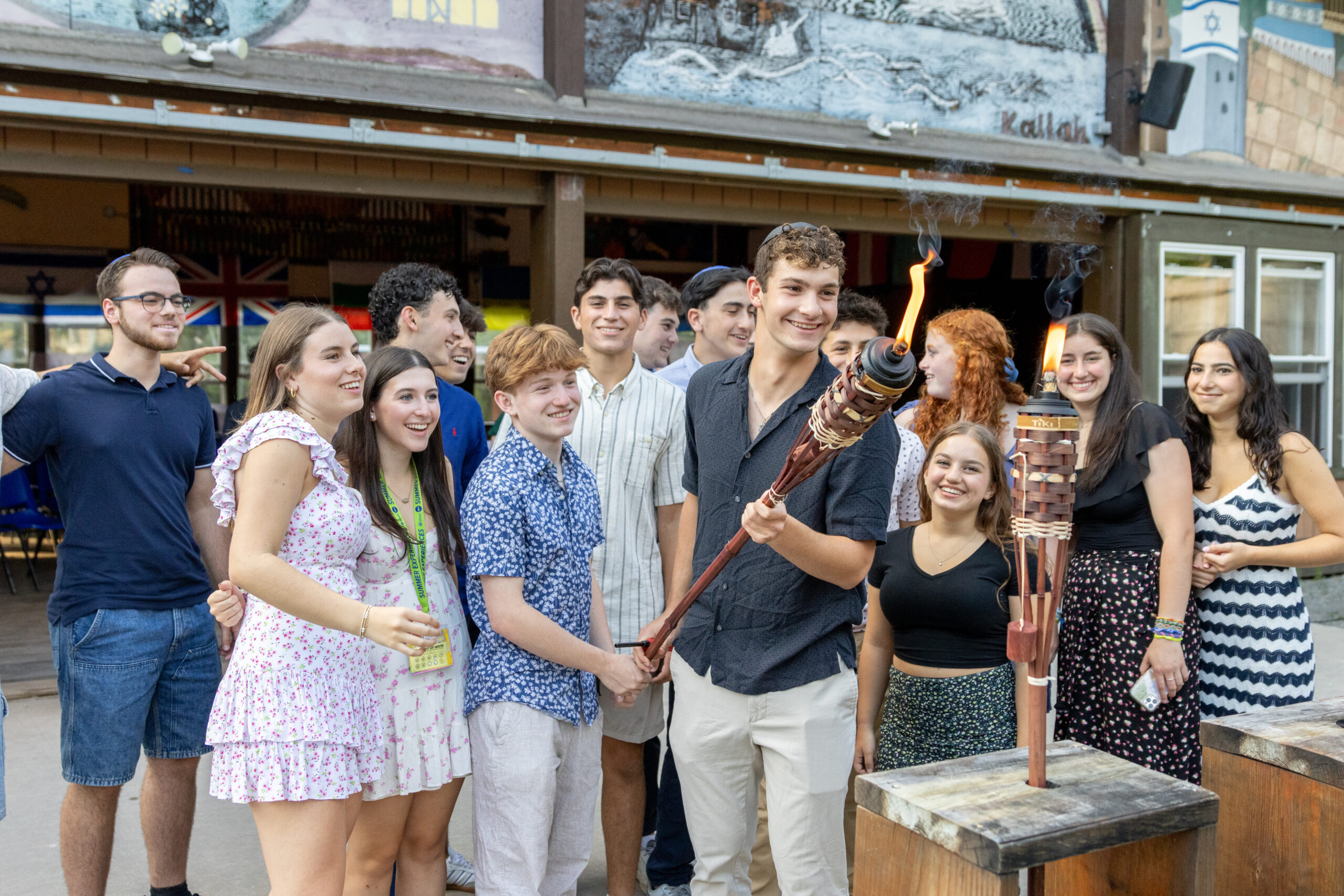 A group of teens gathered together, smiling as one participant holds a lit ceremonial torch, creating an atmosphere of celebration and excitement during a BBYO leadership event.